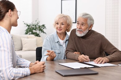 Pension plan. Senior couple consulting with insurance agent at wooden table indoors