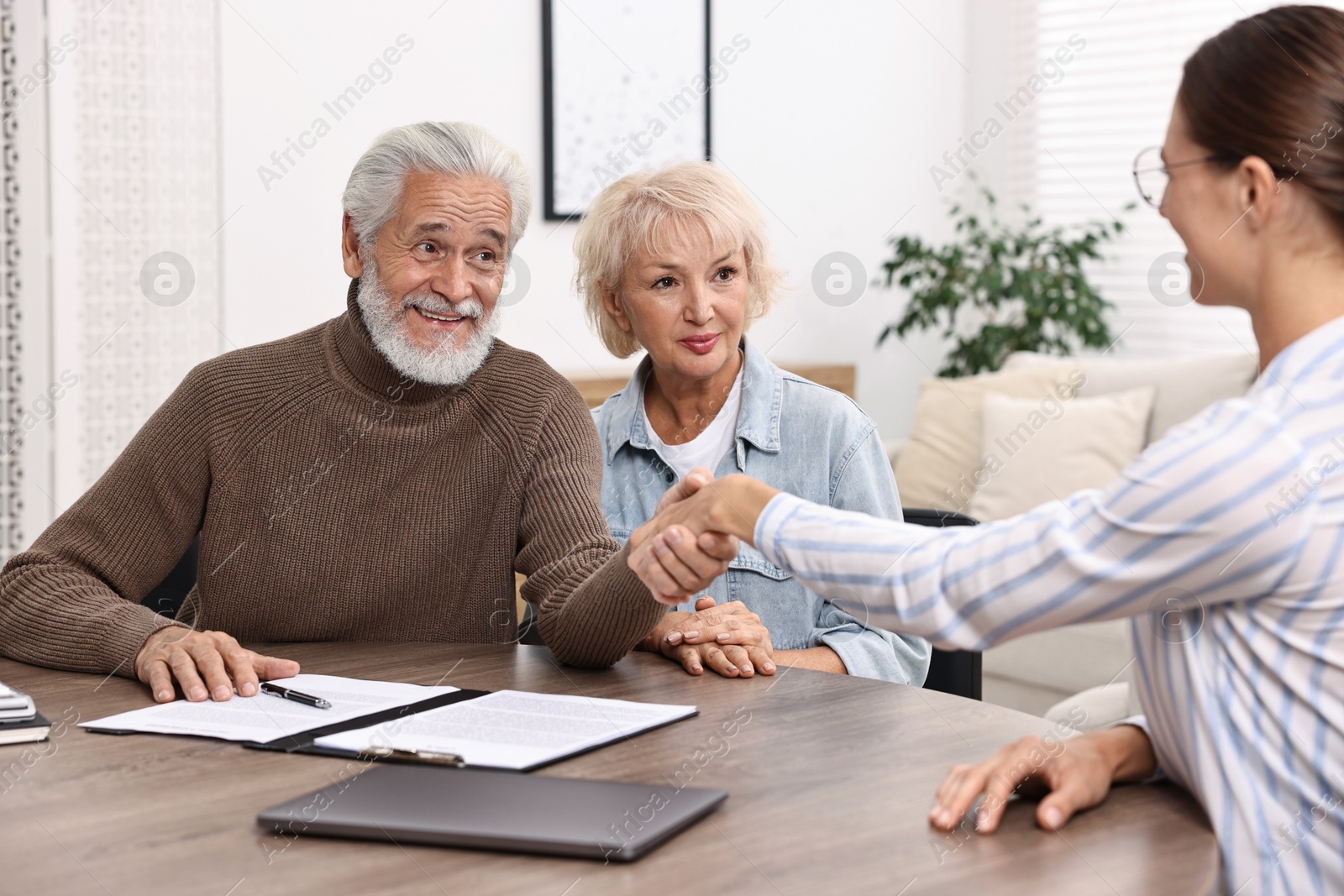 Photo of Pension plan. Senior couple consulting with insurance agent at wooden table indoors