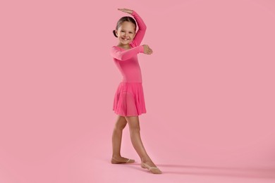 Photo of Little ballerina practicing dance moves on pink background