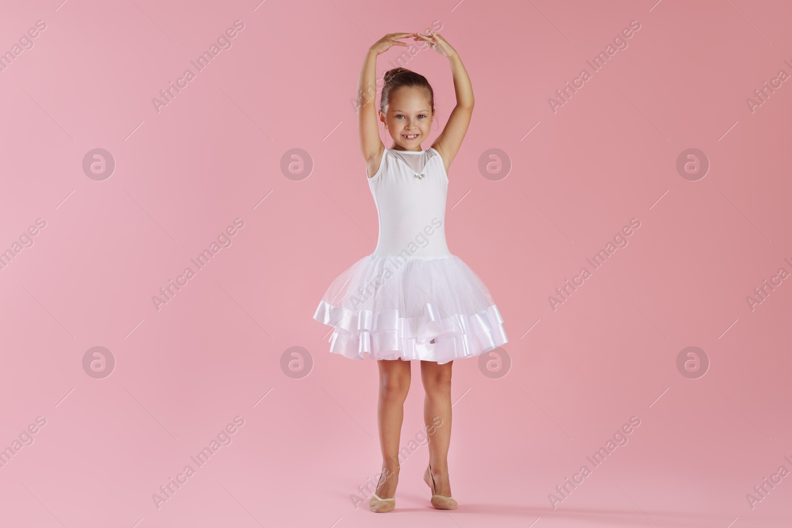 Photo of Little ballerina practicing dance moves on pink background