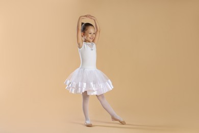 Photo of Little ballerina practicing dance moves on beige background