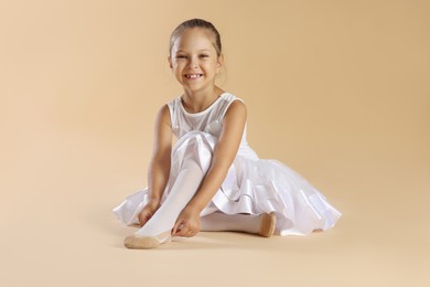 Little ballerina putting on pointe shoes against beige background