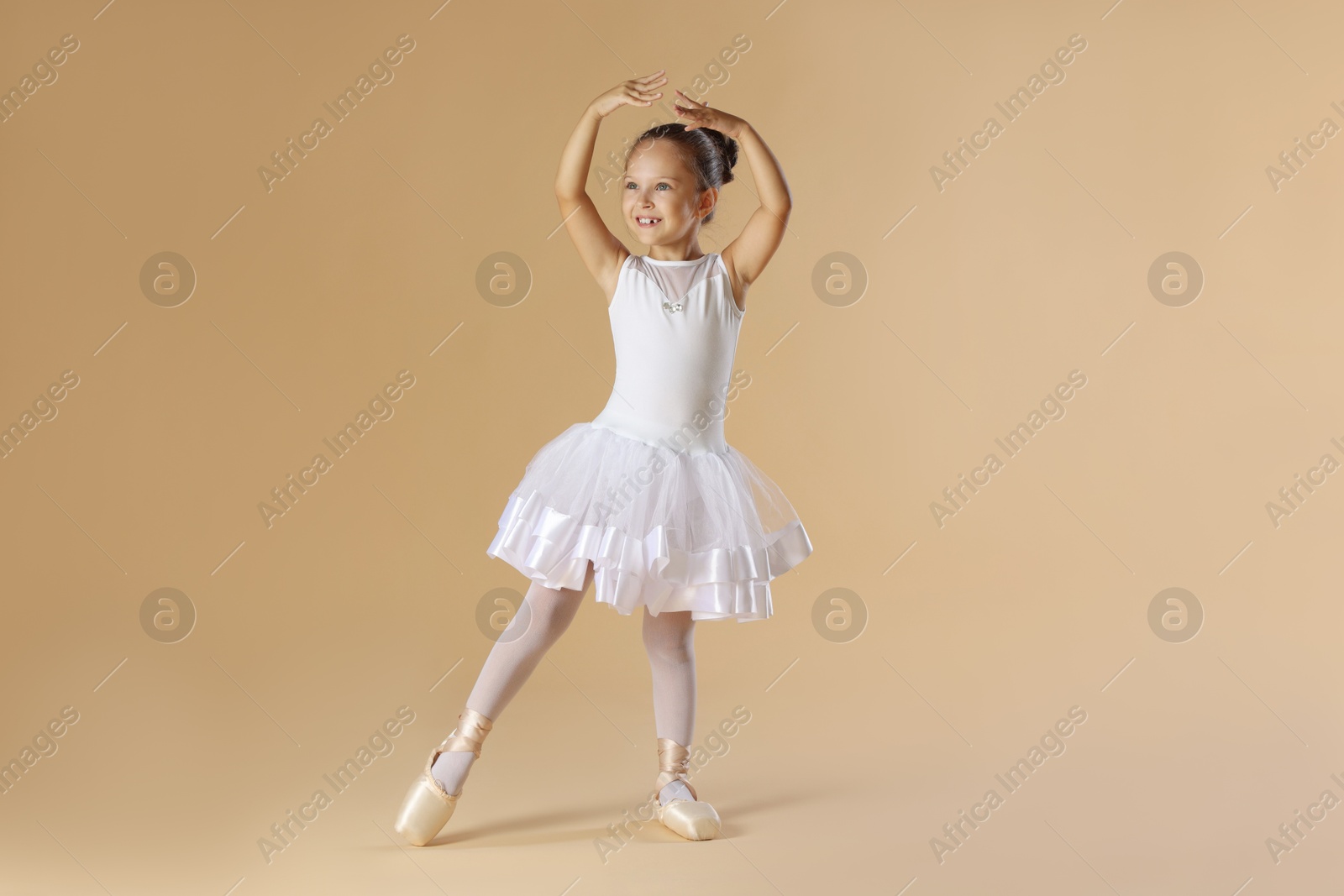 Photo of Little ballerina practicing dance moves on beige background