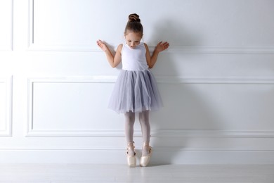 Photo of Little ballerina practicing dance moves near white wall indoors