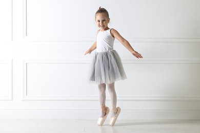 Photo of Little ballerina practicing dance moves near white wall indoors