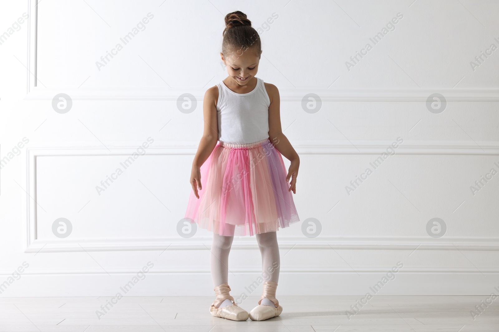 Photo of Little ballerina practicing dance moves near white wall indoors