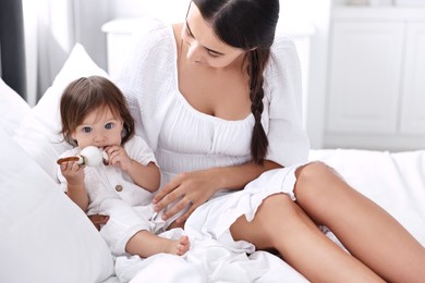 Photo of Beautiful young mother and her cute little baby with rattle on bed at home