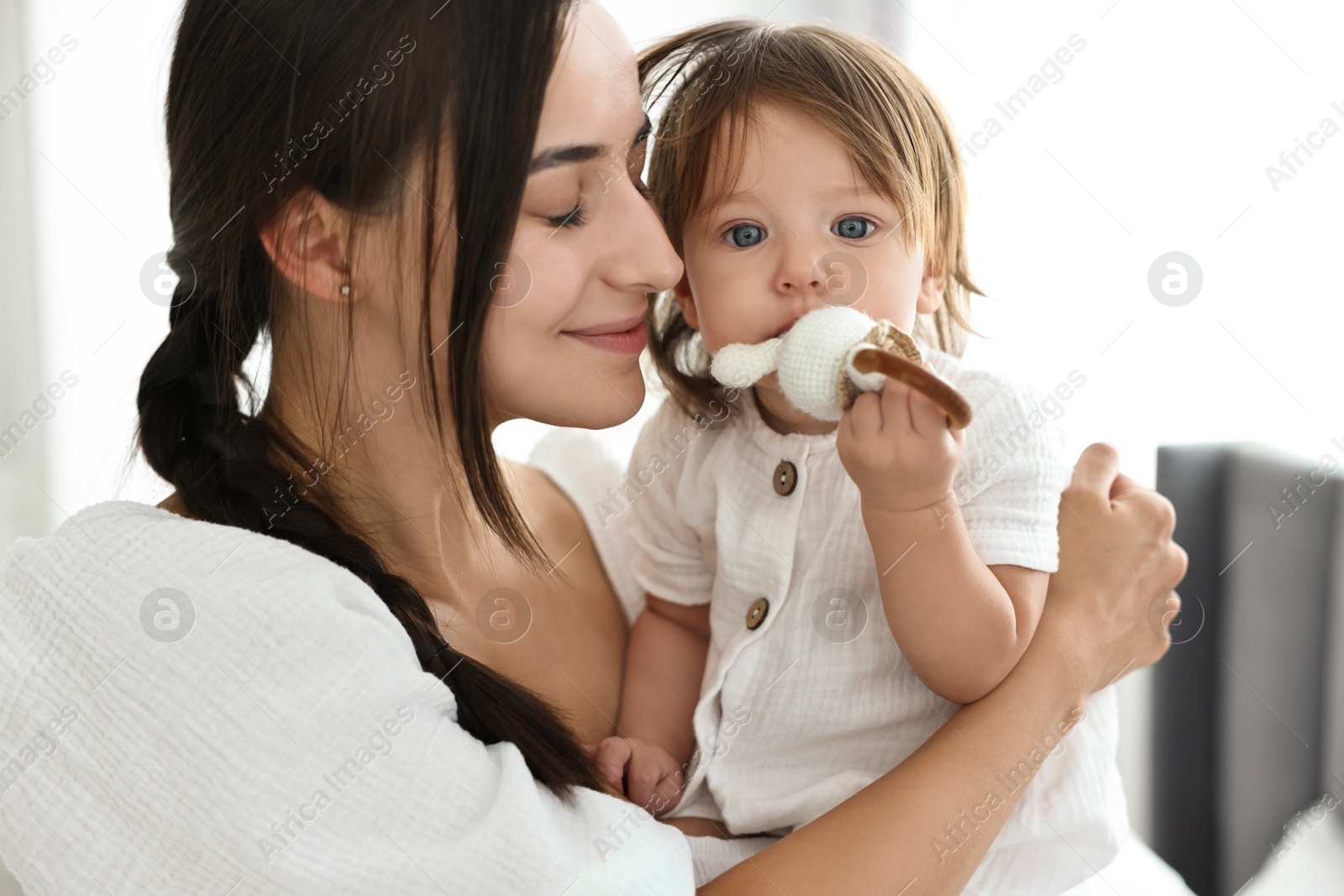 Photo of Beautiful young mother and her cute little baby with rattle indoors