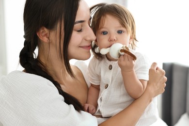 Beautiful young mother and her cute little baby with rattle indoors