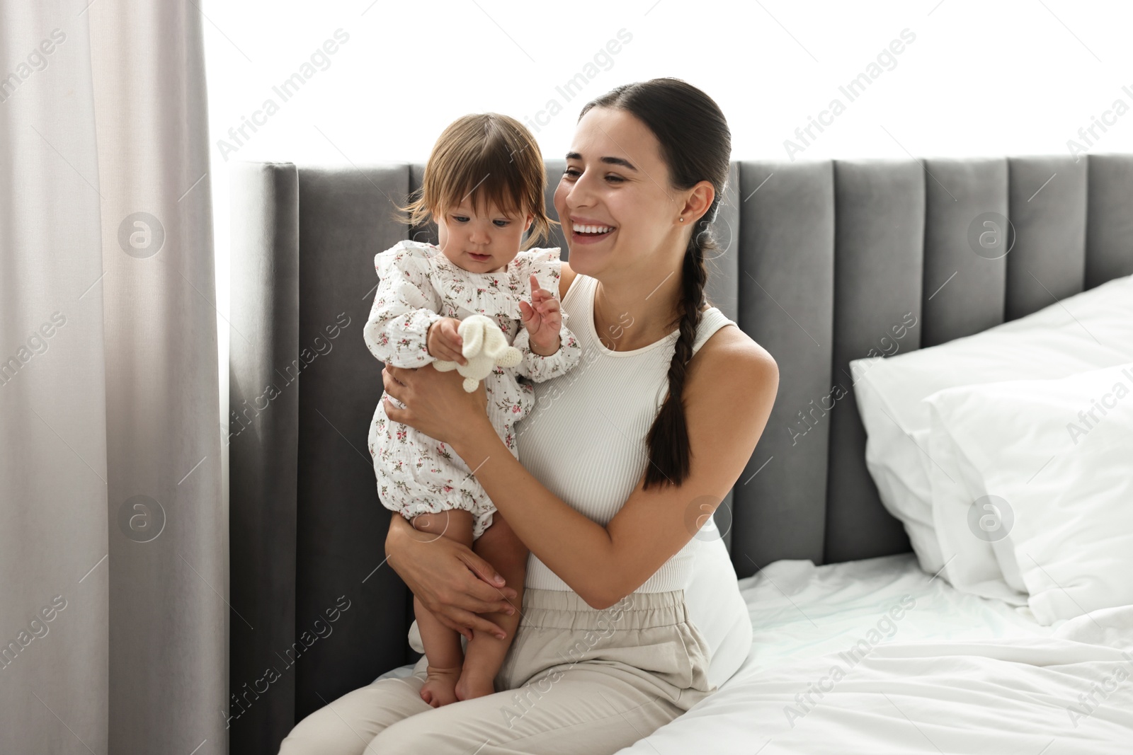 Photo of Beautiful young mother and her cute little baby with rabbit toy on bed at home