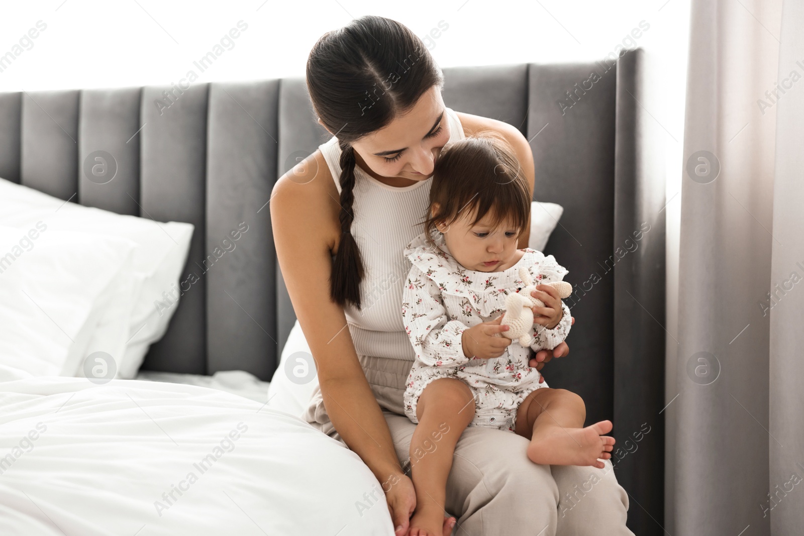 Photo of Beautiful young mother and her cute little baby with rabbit toy on bed at home