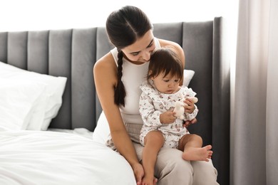 Beautiful young mother and her cute little baby with rabbit toy on bed at home