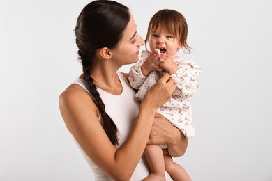 Beautiful young mother and her cute little baby with rattle on light grey background