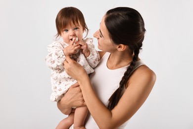 Beautiful young mother and her cute little baby with rattle on light grey background