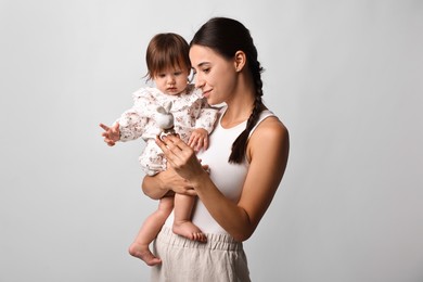 Beautiful young mother and her cute little baby with rattle on light grey background