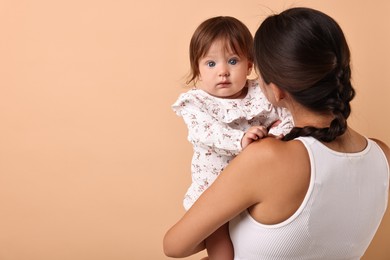 Beautiful young mother and her cute little baby on beige background, space for text