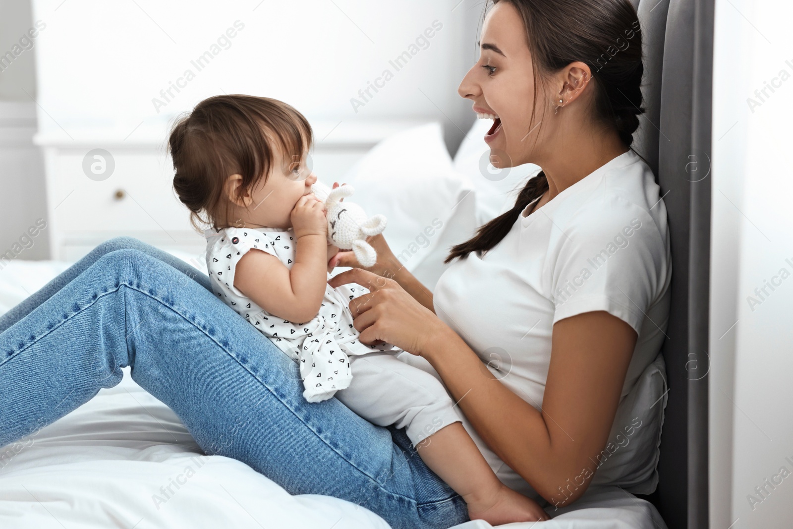 Photo of Beautiful young mother and her cute little baby with rabbit toy on bed at home