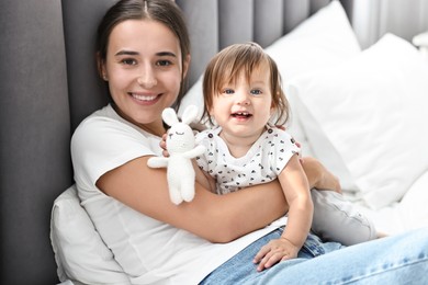 Photo of Beautiful young mother and her cute little baby with rabbit toy on bed at home