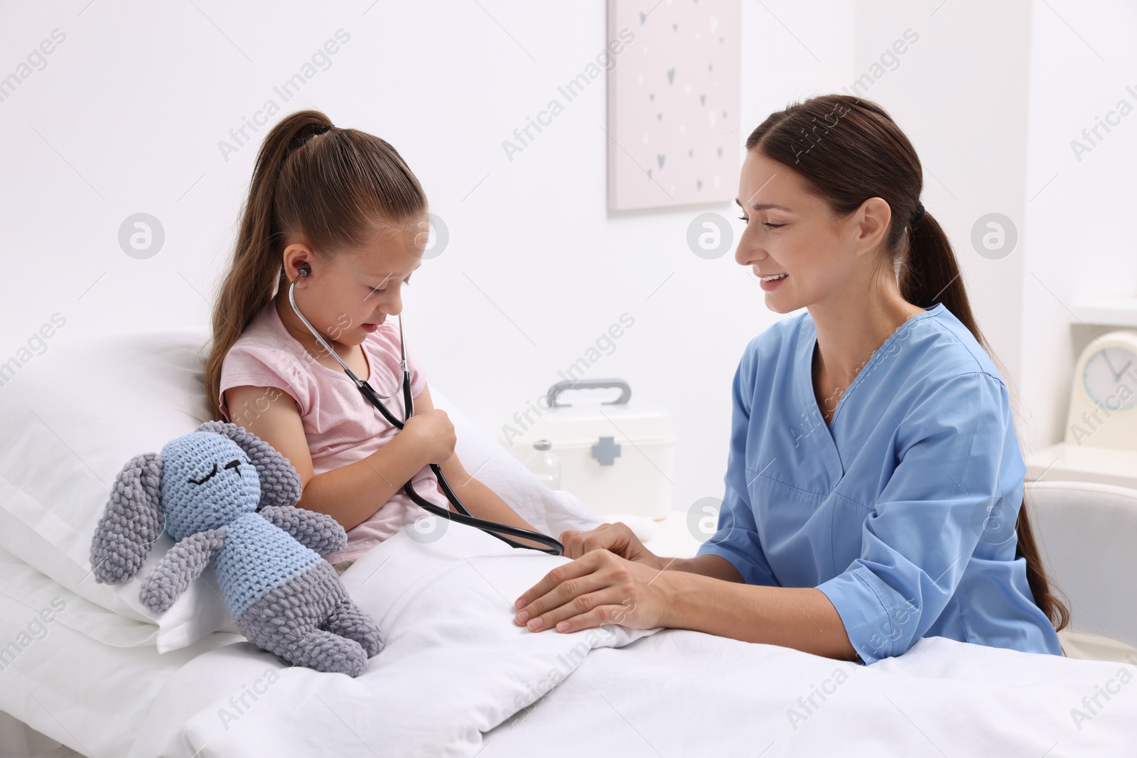 Photo of Doctor examining little girl on bed at hospital