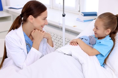 Doctor examining little girl on bed at hospital