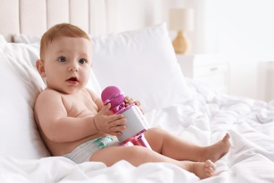 Cute little baby with microphone on bed at home, space for text