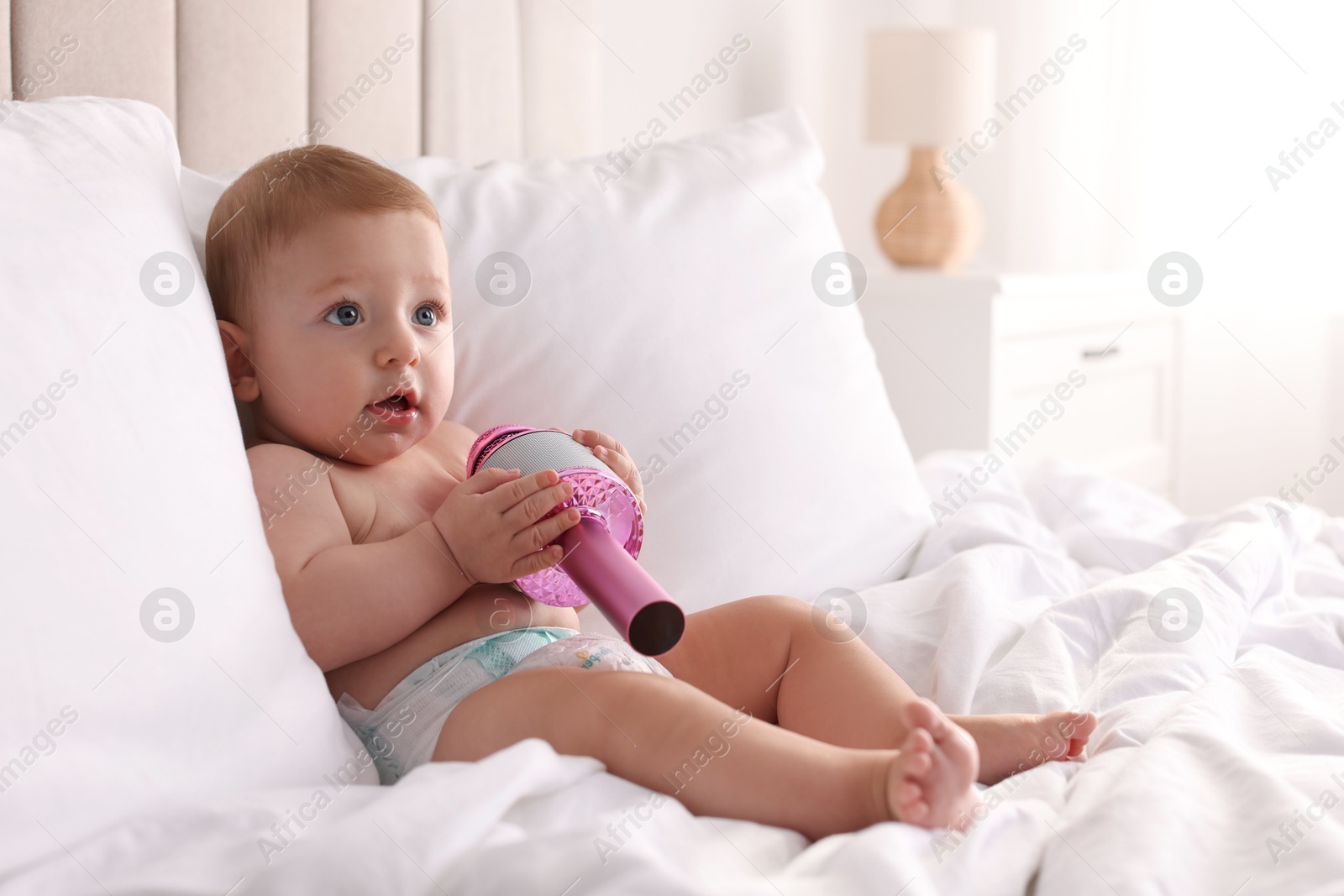 Photo of Cute little baby with microphone on bed at home, space for text