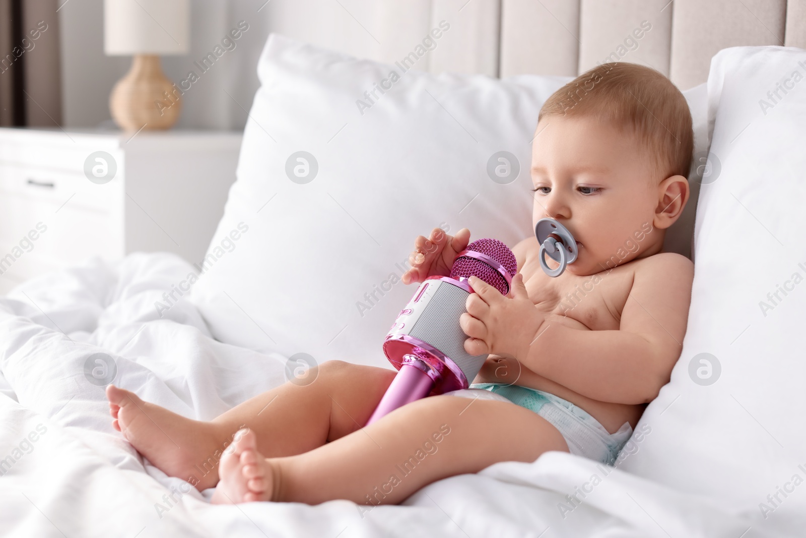 Photo of Cute little baby with microphone and pacifier on bed at home, space for text