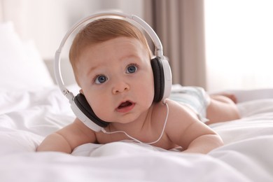 Cute little baby with headphones on bed at home