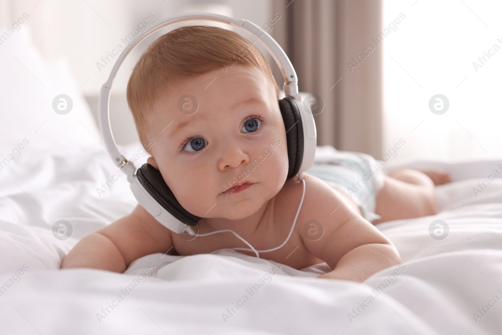 Photo of Cute little baby with headphones on bed at home