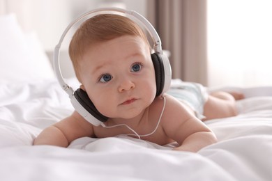 Photo of Cute little baby with headphones on bed at home