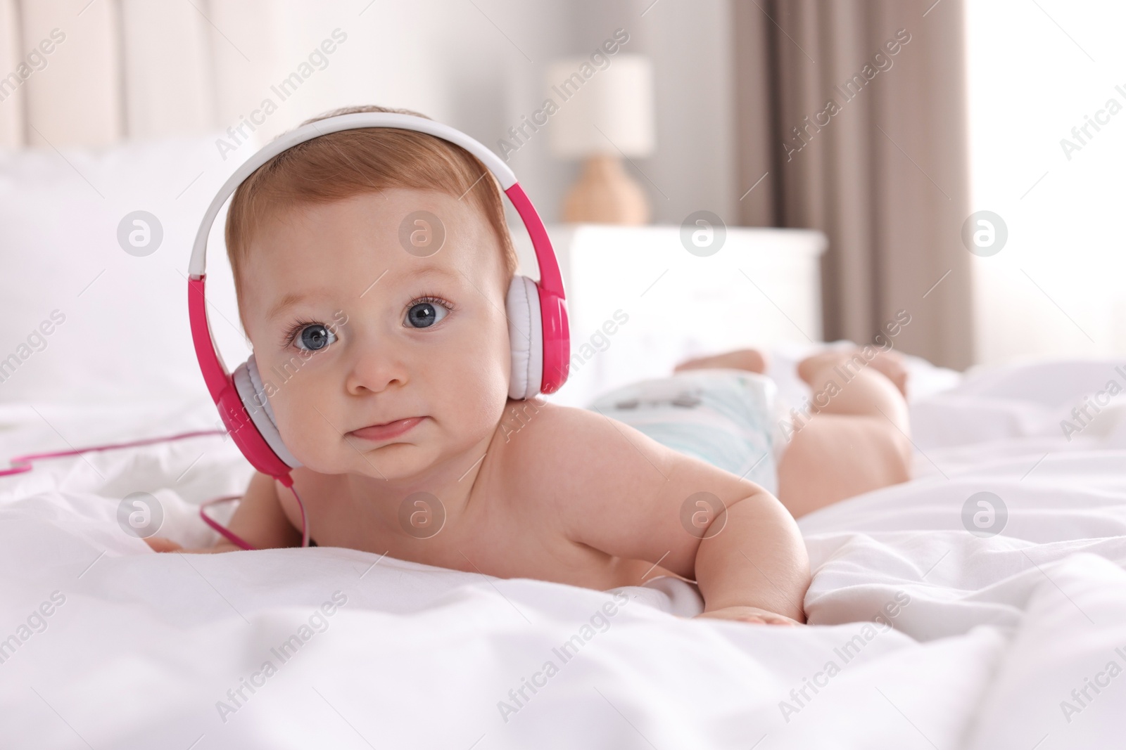 Photo of Cute little baby with headphones on bed at home