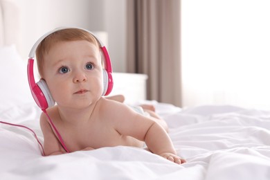 Cute little baby with headphones on bed at home, space for text