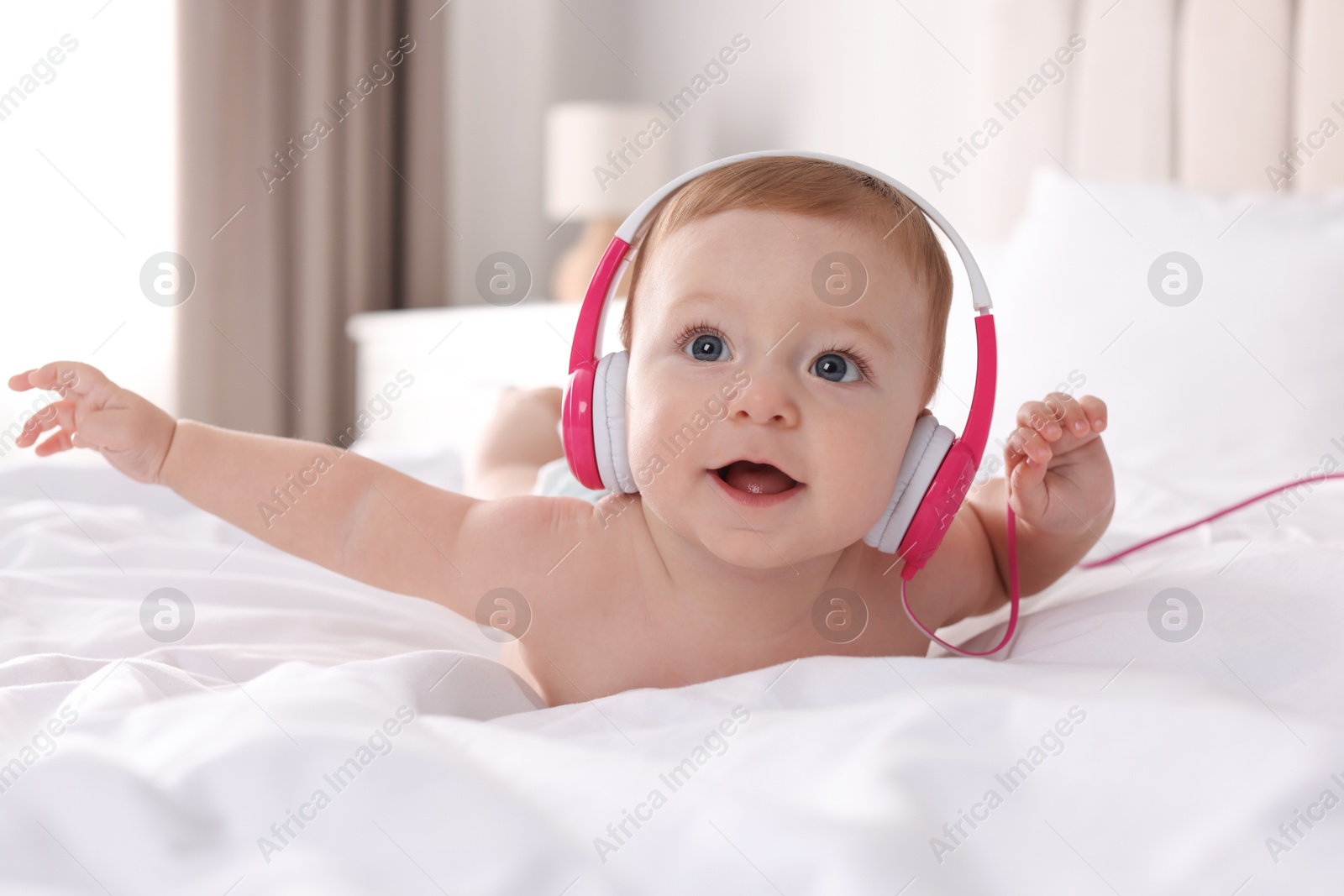 Photo of Cute little baby with headphones on bed at home