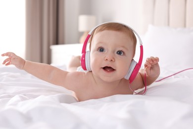 Cute little baby with headphones on bed at home