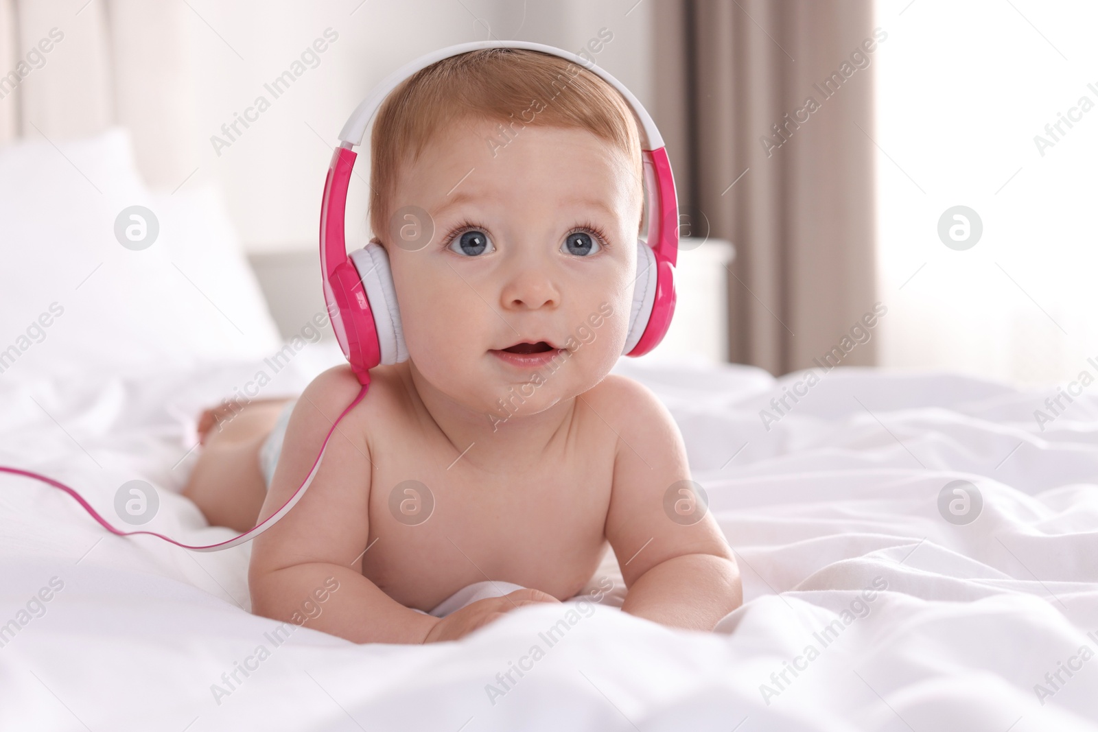 Photo of Cute little baby with headphones on bed at home