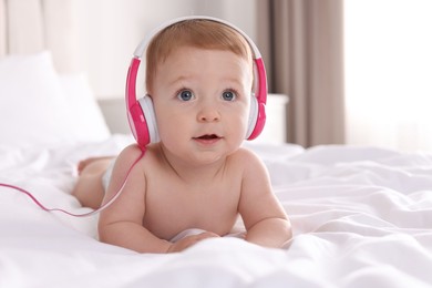 Cute little baby with headphones on bed at home