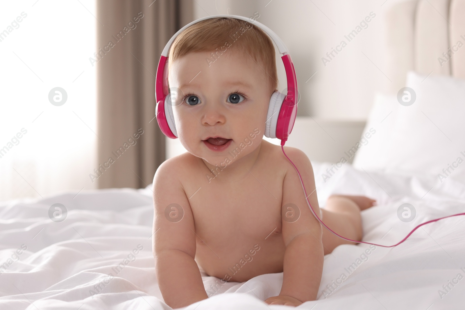 Photo of Cute little baby with headphones on bed at home