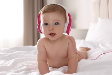 Cute little baby with headphones on bed at home