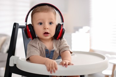 Cute little baby with headphones on high chair at home, space for text