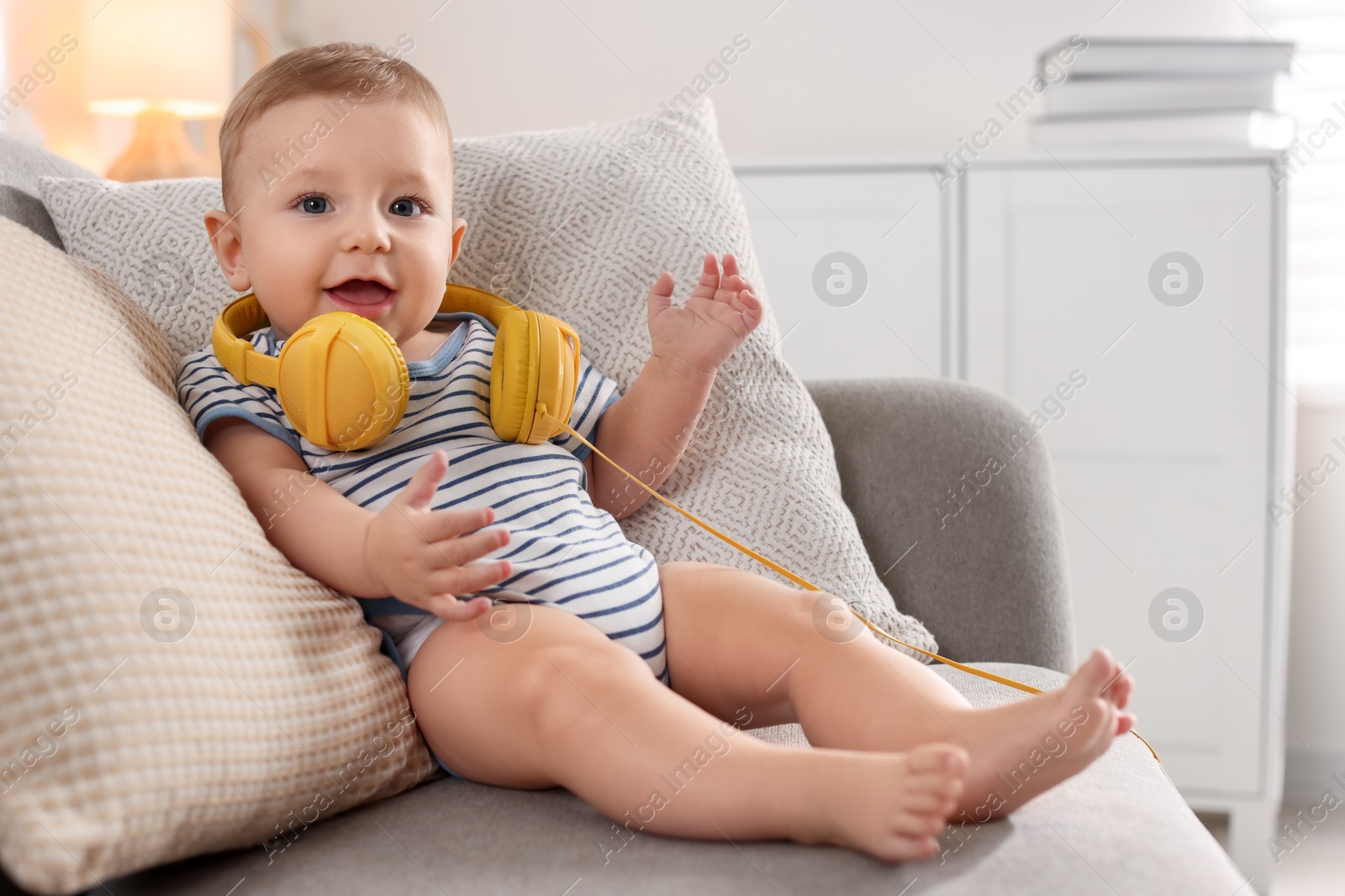 Photo of Cute little baby with headphones on sofa at home, space for text