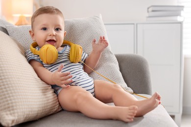 Cute little baby with headphones on sofa at home, space for text