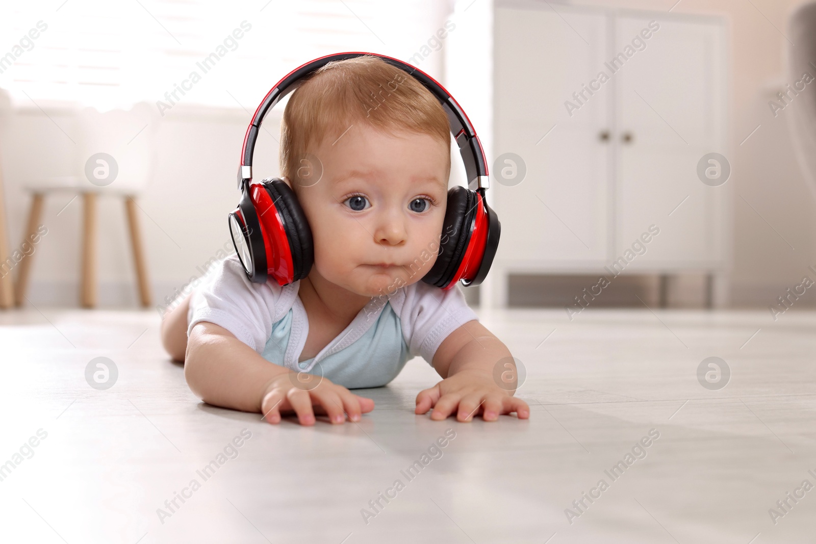 Photo of Cute little baby with headphones on floor at home