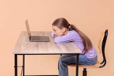 Photo of Girl with incorrect posture using laptop at wooden desk on beige background