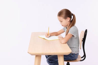 Photo of Girl with correct posture and notebook sitting at wooden desk on white background