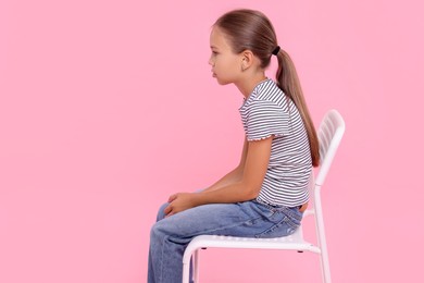 Girl with incorrect posture sitting on chair against pink background