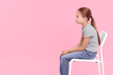 Photo of Girl with incorrect posture sitting on chair against pink background, space for text