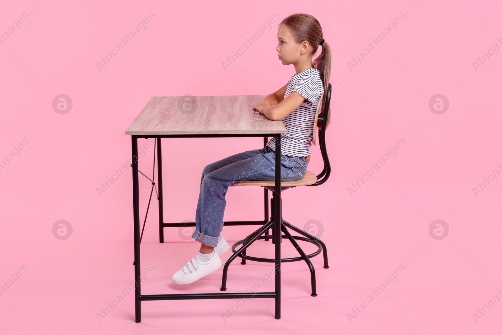 Photo of Girl with correct posture sitting at wooden desk on pink background