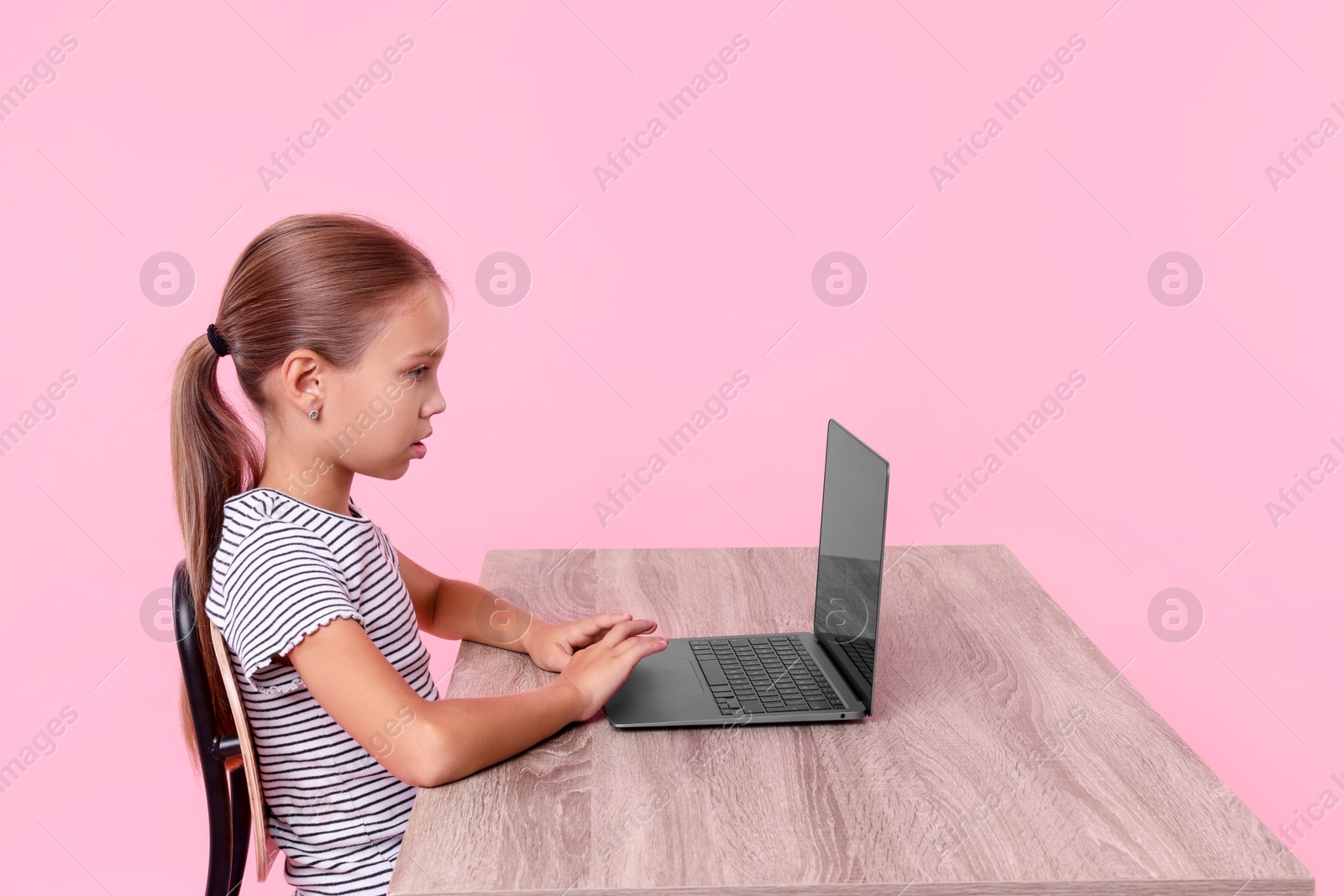 Photo of Girl with correct posture using laptop at wooden desk on pink background