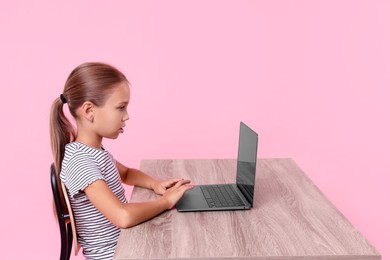 Girl with correct posture using laptop at wooden desk on pink background