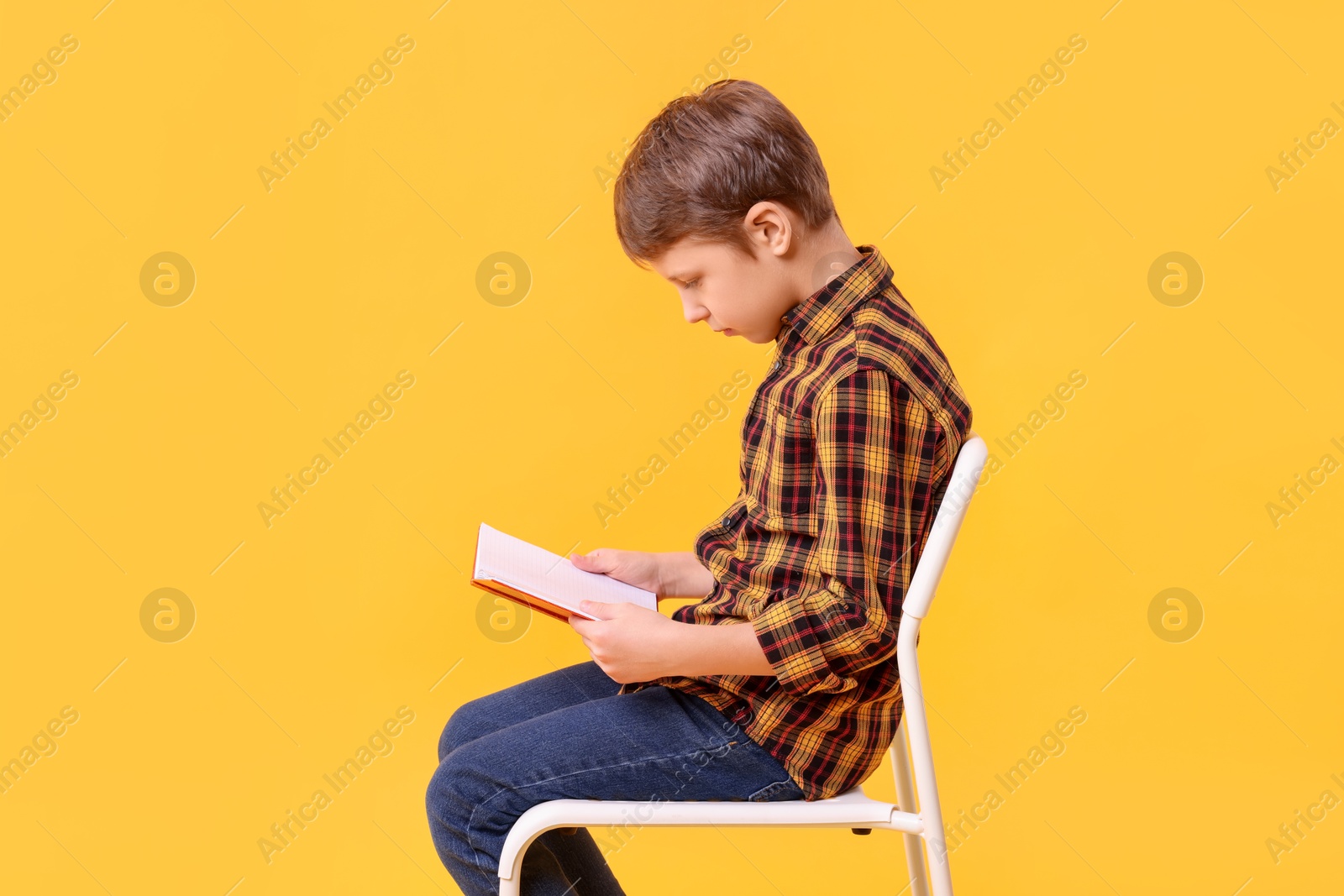 Photo of Boy with incorrect posture reading book on chair against yellow background